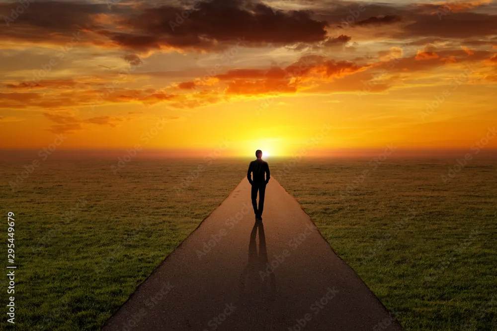 A person walking away from an office building into a bright sunset